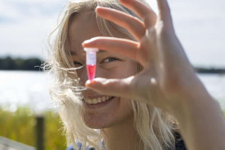 Close-up af en pige, der kigger på et reagensglas med rød farve